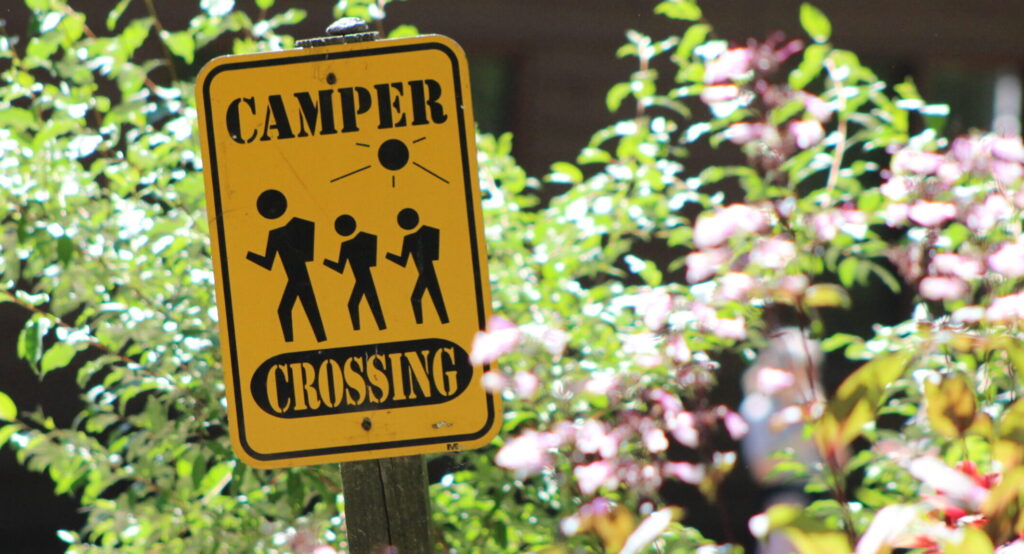 Photo of trees with a sign that says "Camper Crossing"